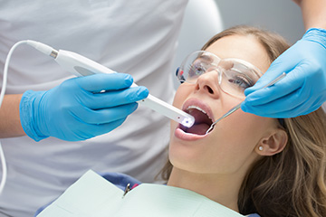 The image shows a dental professional performing an oral examination on a seated patient, with the use of a dental mirror and a probe.