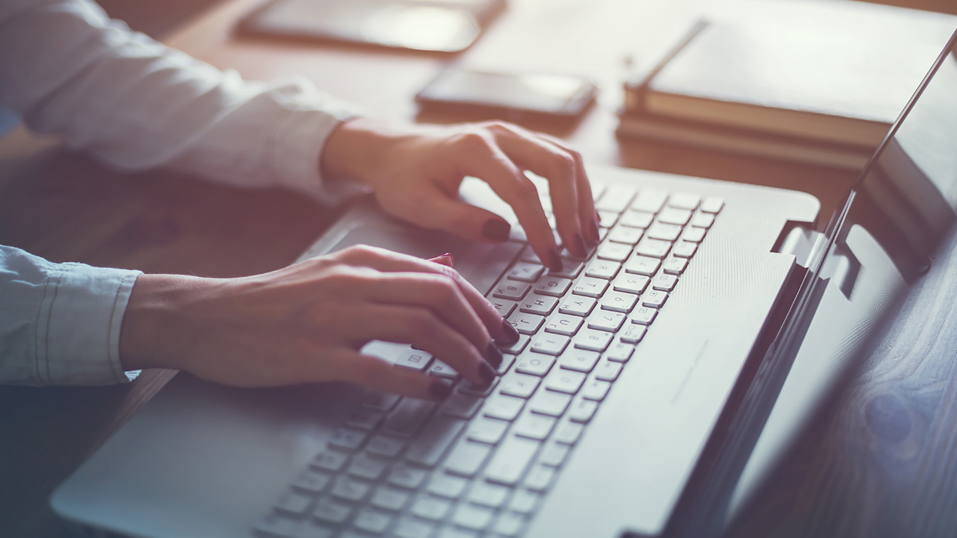 The image shows a person typing on a laptop computer, with a blurred background that suggests an office environment.