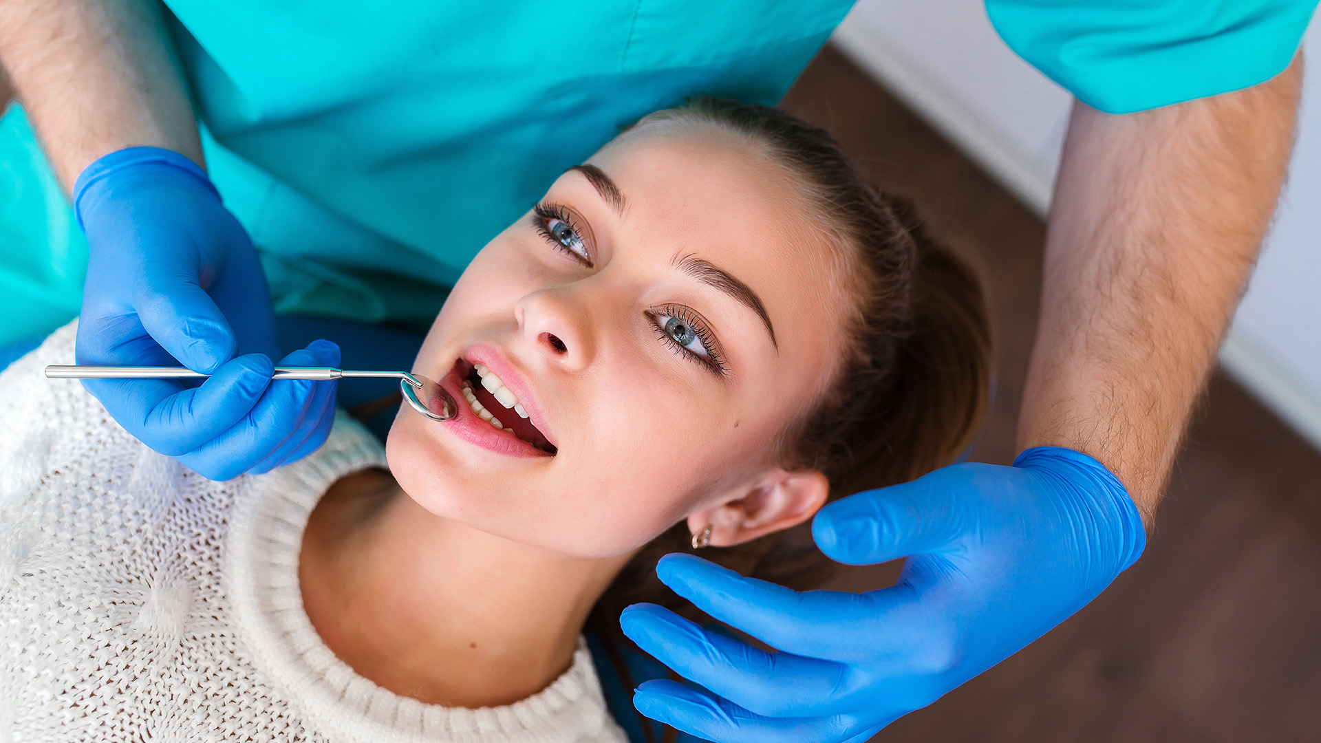 A person receiving dental care, with a dentist performing the procedure while wearing protective gloves and a surgical mask.