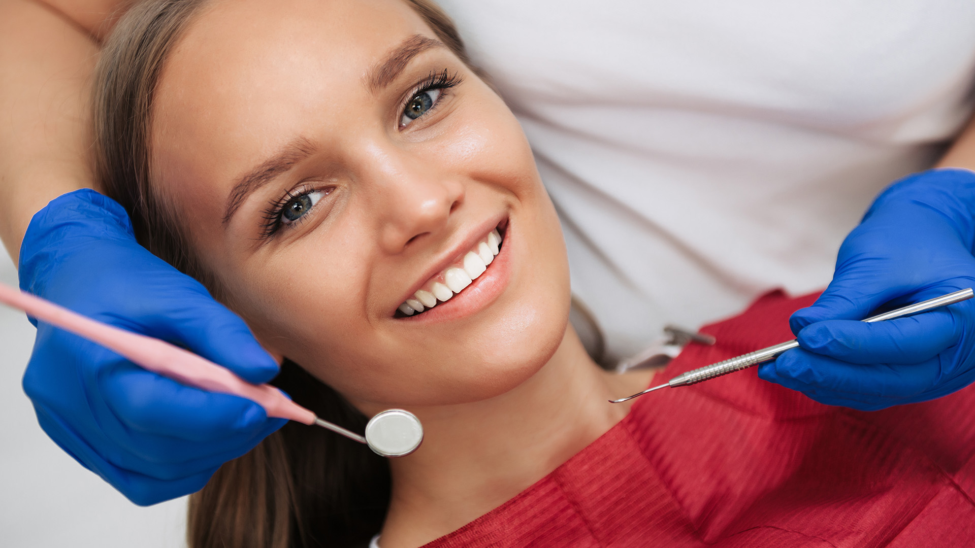 A woman is smiling while sitting in a dental chair, receiving dental treatment.