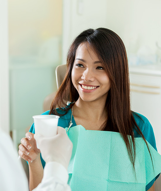 Woman in a dental office, smiling at the camera while holding a cup of coffee.
