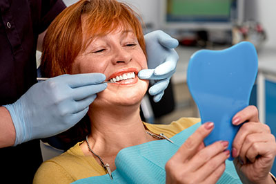 Woman in dental chair receiving dental treatment, smiling at camera with blue teeth guard.