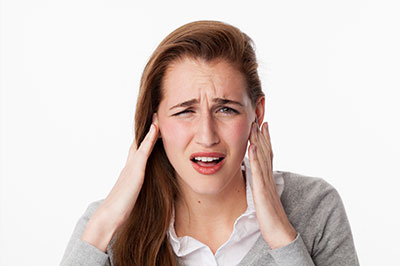 A young woman with a surprised expression is holding her hand to her ear, possibly indicating discomfort or pain.