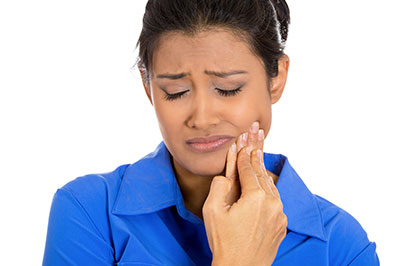 Woman with a concerned expression, holding her face and looking downwards.