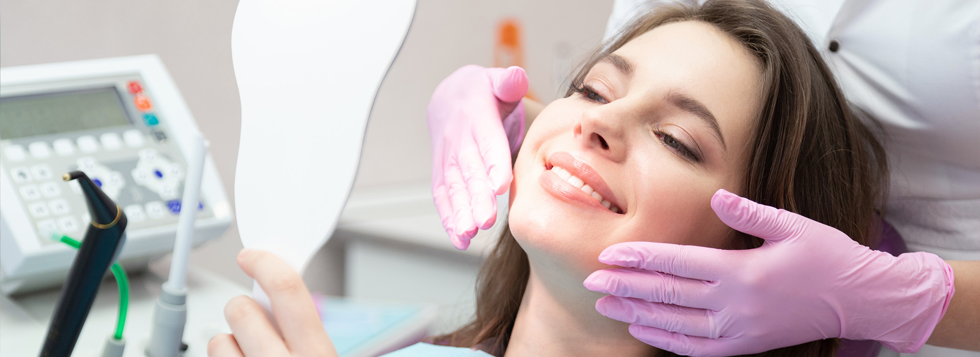 A woman is seated in a dental chair, smiling, while receiving dental care.