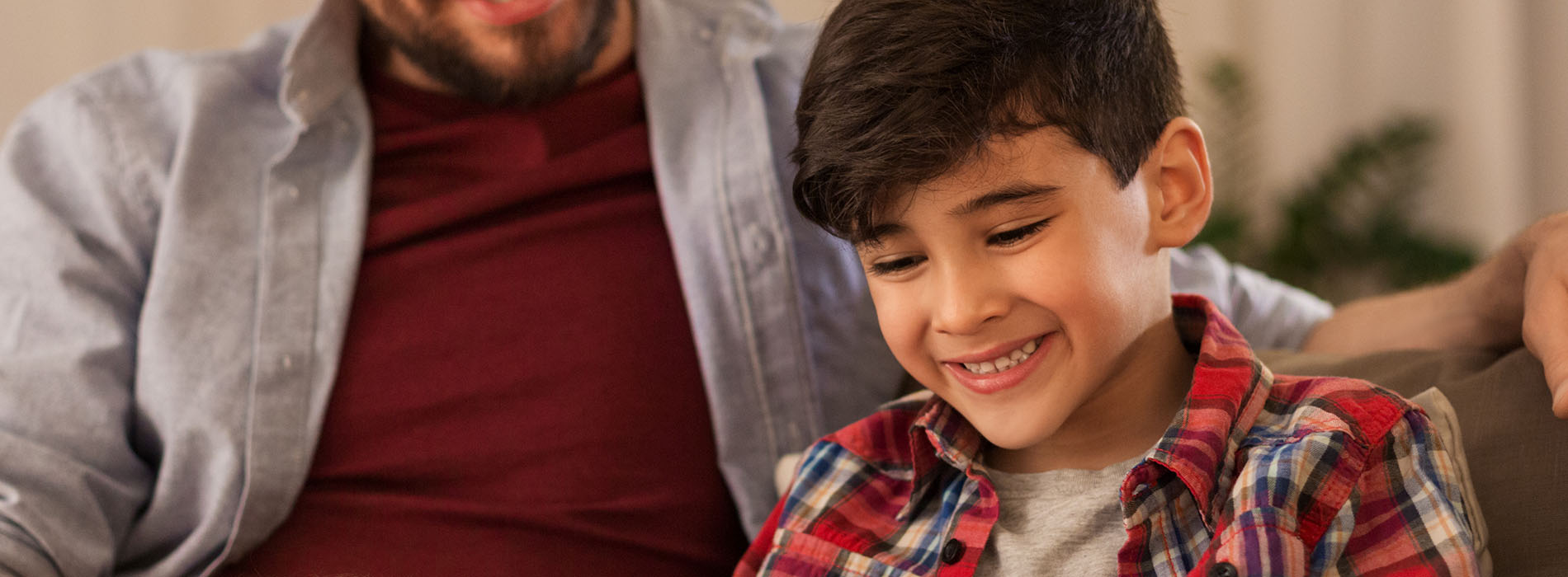 Adult and child sitting on couch, smiling at camera.