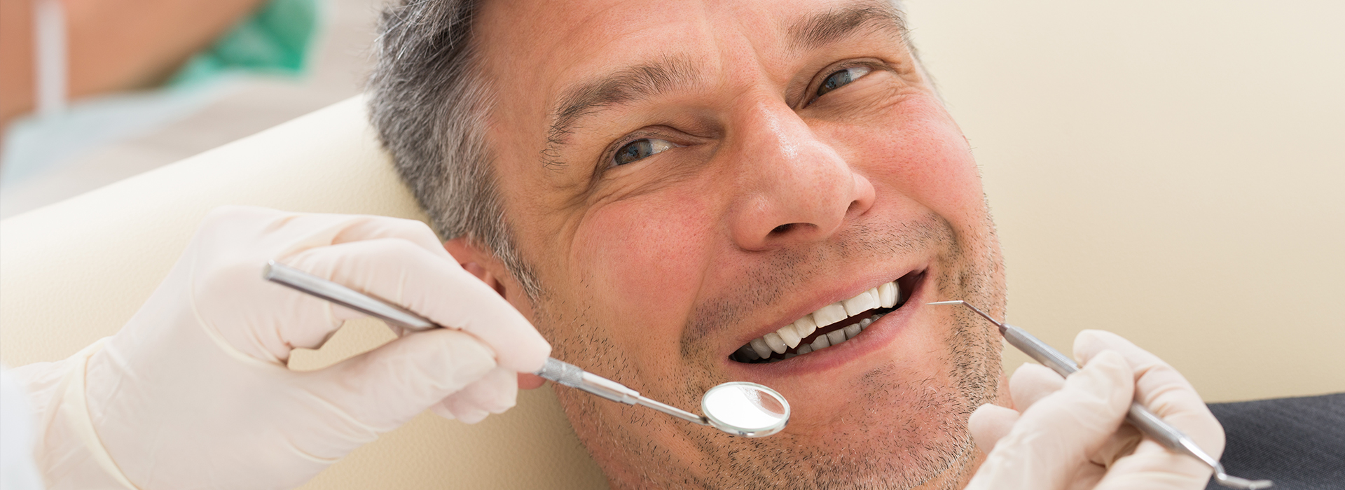 A man in a dental chair receiving dental care, with the dentist performing a procedure and smiling.