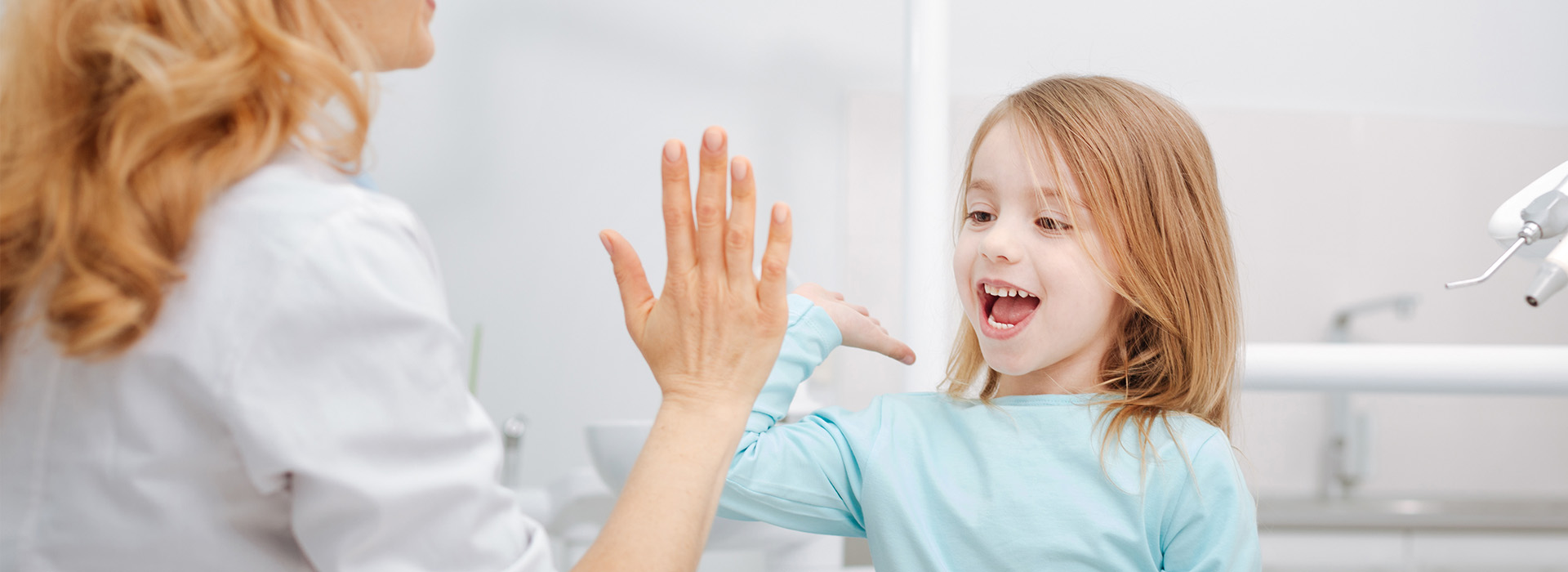 A woman and a young girl in a dental office, with the woman smiling at the child.