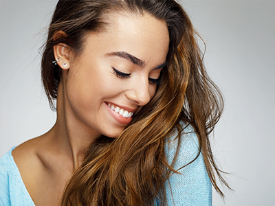 A smiling woman with long hair, wearing a blue top, against a plain background.