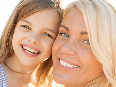 A woman and a young girl smiling at the camera, with the woman appearing to be the mother of the child.