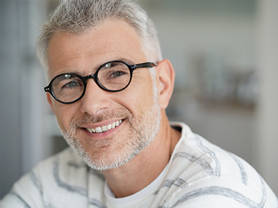 The image features a man with gray hair, wearing glasses and a white shirt, smiling at the camera.